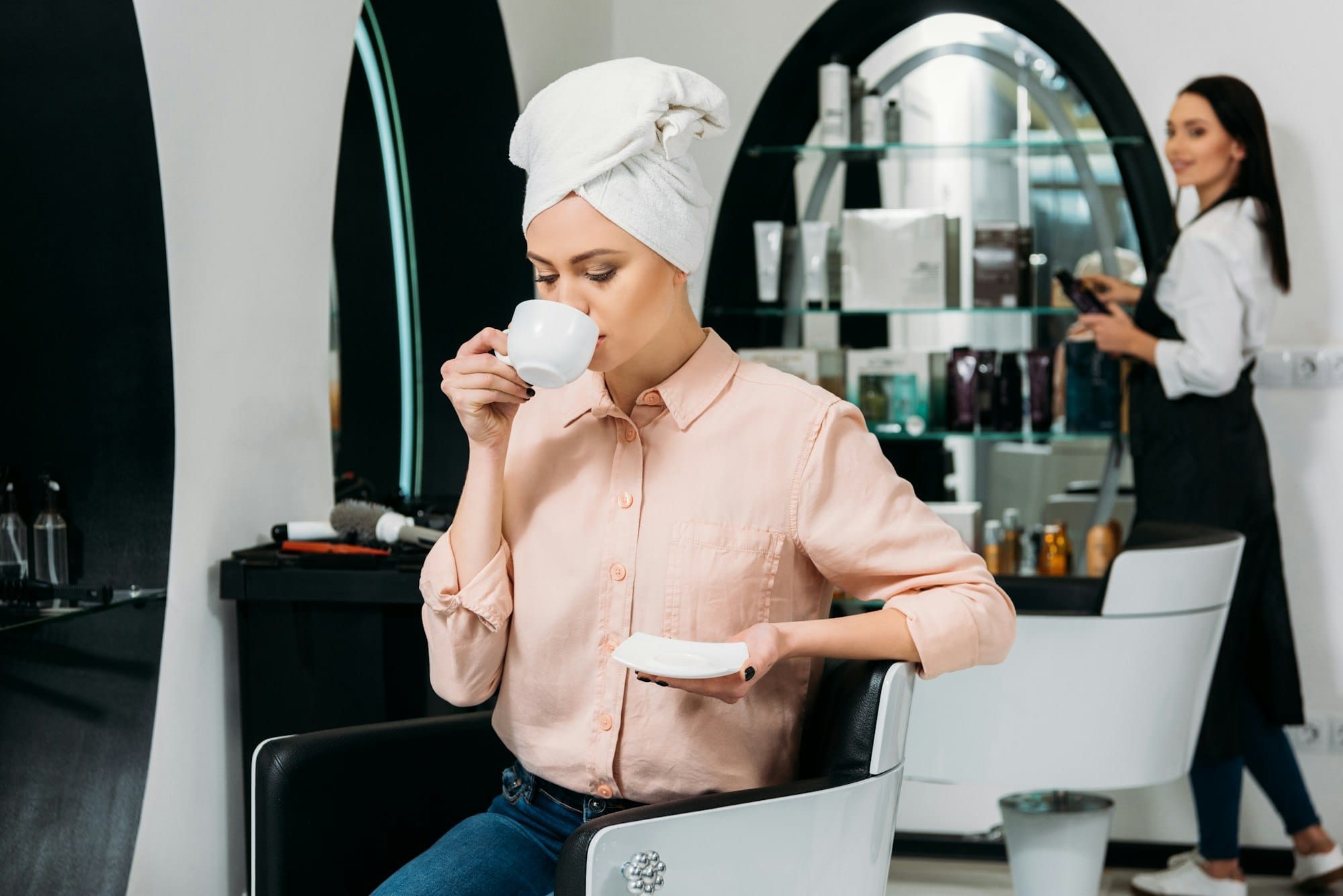 customer with towel on head sitting and drinking coffee in hair salon